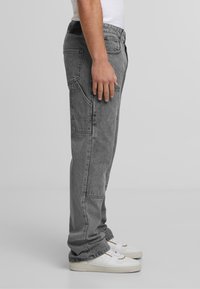 Graue Denim-Cargohose mit Seitentaschen, lässigem Schnitt und sichtbaren Steppnähten, kombiniert mit weißen Sneakers.