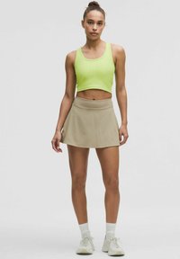 Helle limettengrüne, cropped Tanktop und beiger Skort, mit einer taillierten Taille und einem fließenden Rock. Kombiniert mit weißen Knöchelsocken und Sneakers.
