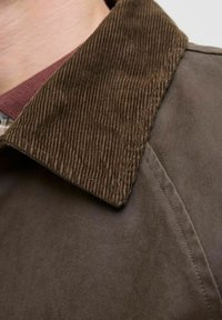 Giacca marrone con colletto in corduroy. Il tessuto principale è liscio con una finitura opaca, che mostra cuciture precise e un design strutturato.