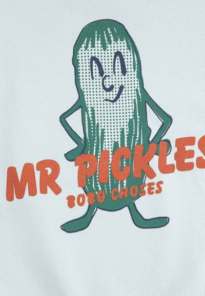 Personnage de cornichon souriant de dessin animé, les mains sur les hanches, se tenant au-dessus du texte « MR PICKLES 7800 CHOSES » en lettres orange grasses.