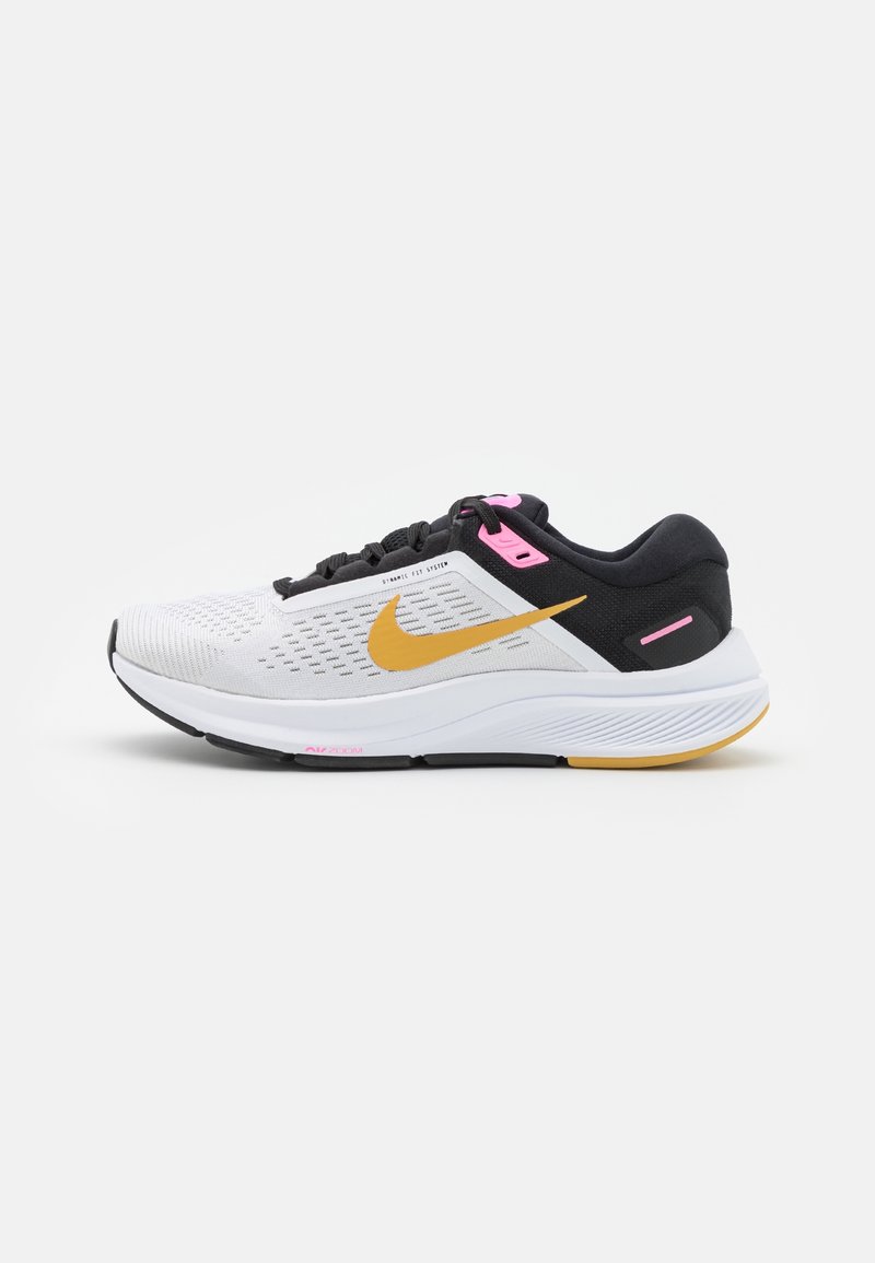 Scarpa da ginnastica bianca con accenti neri e rosa, caratterizzata da una tomaia in mesh traspirante, suola ammortizzata e un audace logo Nike giallo.