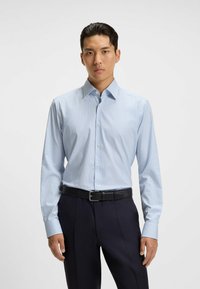 Camicia a scacchi azzurro chiaro con maniche lunghe, colletto bottonato e vestibilità slim. Abbinata a pantaloni scuri e a una cintura nera.