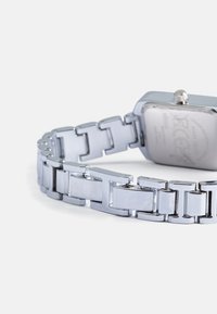 Relógio de pulso em aço inoxidável prateado com um mostrador retangular, design de bracelete em elos e um acabamento polido. Apresenta uma coroa de lado.