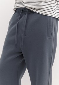 Nahaufnahme einer Person, die graue Sweatpants mit Kordelzugbund und seitlicher Tasche trägt, kombiniert mit einem weiß-schwarz gestreiften Shirt.