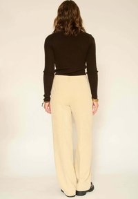 Haut marron à manches longues côtelé assorti à un pantalon beige taille haute à jambe large avec une finition texturée et des chaussures noires.