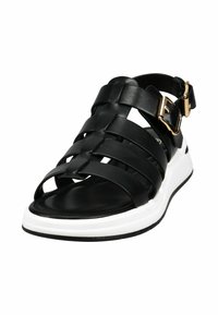 Black leather sandal with woven straps, adjustable ankle buckle, white sole, and flat design for comfort.