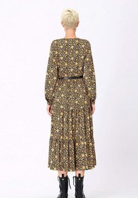 Robe longue à manches longues avec un fond noir décoré de motifs jaunes et bleus, une jupe à volants, et une taille cintrée par une ceinture noire.
