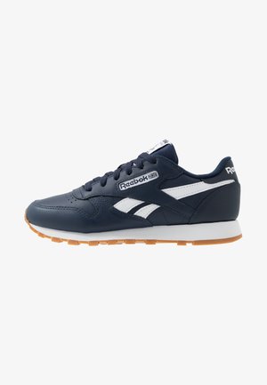 Baskets Reebok bleu marine avec des bandes blanches sur les côtés, semelle en caoutchouc, lacets, et logo de la marque sur le côté et le talon.