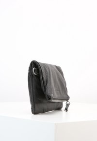 Borsa in pelle nera con superficie testurizzata, dotata di patta pieghevole, dettagli in argento e chiusura con zip nella parte inferiore.