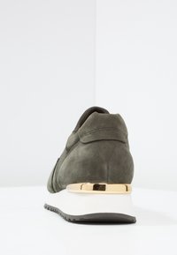 Baskets en daim vert avec une forme arrondie et un accent métallique doré au niveau du talon, dotées d'une semelle en caoutchouc blanche et d'une finition texturée.