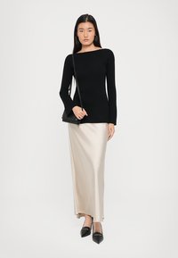 Crna rebrasta bluza dugih rukava, kremasta satin midi suknja, crne cipele s oštrim nosom i mala crna torbica preko ramena. Jednostavan, prilagođen dizajn.