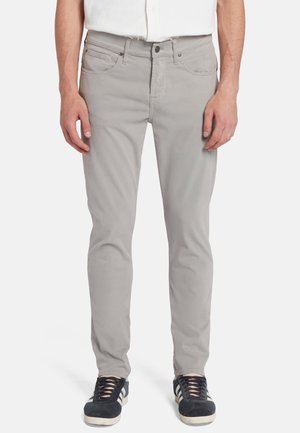 Jeans in cotone grigio chiaro con una vestibilità slim, caratterizzati da cinque tasche, chiusura con zip e cuciture a contrasto, abbinati a sneaker scure.