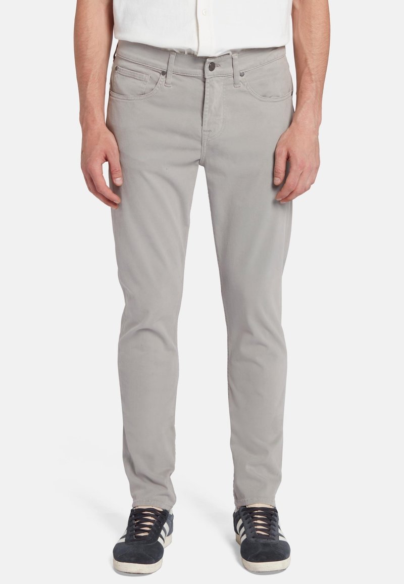 Jeans en coton gris clair avec une coupe slim, dotés de cinq poches, d'une fermeture éclair et de coutures contrastantes, associés à des baskets sombres.
