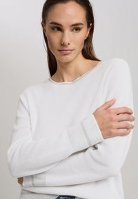 Weißer, gerippter Strickpullover mit runder Ausschnitt und langen Ärmeln, der gestreifte kontrastierende Akzente an den Bündchen aufweist. Glatte Textur.
