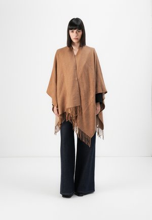 Poncho intrecciato marrone con dettagli in frange, caratterizzato da un motivo testurizzato. Abbinato a jeans a campana scuri. Tessuto morbido e silhouette comoda.