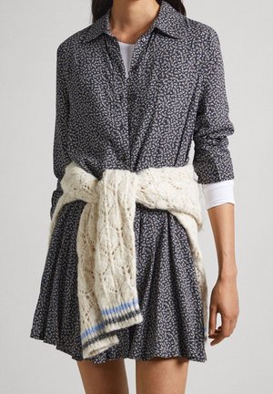 Granatowa sukienka w kwiatowy wzór z kołnierzykiem i zapinana na guziki, zestawiona z kremowym, teksturowanym, dzianym szalem. Plisowana spódnica sięga powyżej kolana.