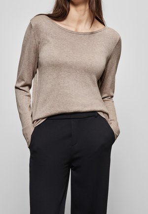 Lysbrun, langærmet sweater med bred halsudskæring og ribbede manchetter, parret med sorte, skræddersyede bukser med sidelommer.