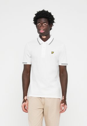 Chemise polo blanche avec col et patte de boutonnage à trois boutons. Accents gris sur le col et les manches, avec un logo d'oiseau jaune sur la poitrine.
