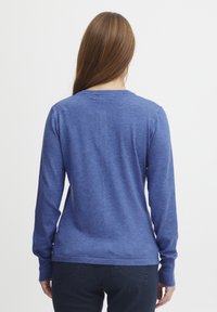 Bluza s dolgimi rokavi, modra, iz mehkega materiala, s klasičnim izrezom, ki ima gladko teksturo in rebraste manšete. Zadnji pogled prikazuje sproščen kroj.