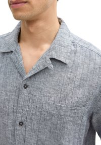 Graues Hemd mit Knöpfen und vertikalen Streifen, aus strukturiertem Stoff. Verfügt über eine Tasche, einen Umlegekragen und dunkle Knöpfe.