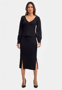 Schwarzes, geripptes Strick-Zweiteiler-Set mit V-Ausschnitt, langärmligem Oberteil und Midirock mit seitlichen Schlitzen, kombiniert mit schwarzen High Heels.