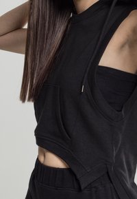 Zwarte cropped hoodie van zachte stof, met een zak aan de voorkant, een capuchon en uitsnijdingen aan de zijkanten voor een ontspannen pasvorm. Gevoelige afwerking.