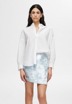 Chemise blanche à manches longues, assortie à une jupe bleu clair brillante à motif floral dans des nuances de bleu variées.