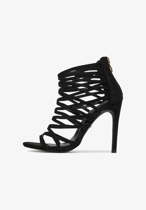 Čierne semišové sandále na vysokom opätku s prekríženými remienkami, otvorenou špičkou a zipsom na zadnej strane. Majú elegantný, špicatý opätok.