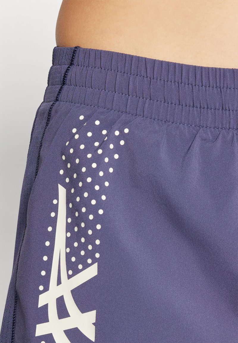 Shorts de sport bleu marine avec une taille élastique, ornés d'un logo blanc et d'un motif à pois d'un côté. Le tissu semble lisse et léger.