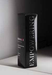 Czarny prostokątny pojemnik na serum o błyszczącej powierzchni. Posiada wyraźny biały tekst: "SERUM WZMACNIAJĄCE" i "ZASILANIE ENERGIĄ". Smukły, nowoczesny design.