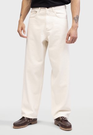 Cream-colored wide-leg jeans in thick fabric with a smooth texture. Features include a button closure and front pockets, worn with dark shoes.