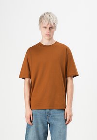 Brun bomulds t-shirt med korte ærmer, rund halsudskæring og en afslappet pasform, parret med lyseblå denim jeans.