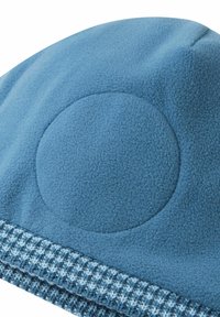 Niebieska poliestrowa czapka z okrągłym akcentem na czubku oraz teksturowanym, wzorzastym dzianinowym paskiem u podstawy. Miękki materiał na całej powierzchni.