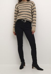 Beżowy sweter w paski z długimi rękawami, czarne dopasowane jeansy oraz czarne szpiczaste botki na obcasie z teksturowaną powierzchnią.