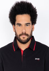 Svart polo skjorte med røde aksenter, med knappekrage og brodert logo på venstre side. Strukturert stoff, kort ermer.