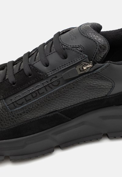 Black sneaker featuring a mix of textured leather and suede, a prominent zipper closure, and a thick, cushioning sole for support.