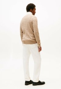 Maglione beige a maglia con orlo e polsini a costine, abbinato a pantaloni bianchi e scarpe nere, visto da dietro.