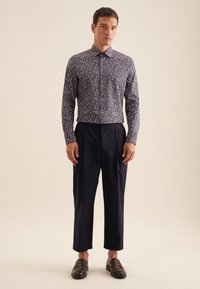 Marineblauwe bloemetjesoverhemd met lange mouwen, gecombineerd met donkere geplooide broeken en bruine loafers.