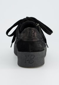 Baskets en suede noir avec des lacets plats noirs, une semelle épaisse grise texturée et un logo embossé au niveau du talon. Le design est simple et moderne.