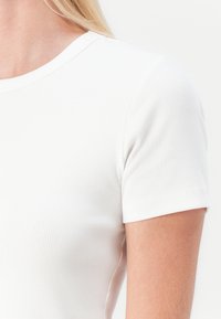 Vit ribbad t-shirt med kort ärm som har en rund halsringning och en figurnära design, med en slät textur utan synliga dekorationer.