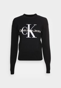Černý svetr z pleteného materiálu, s kulatým výstřihem, dlouhými rukávy a výrazným bílým logem: "Calvin Klein Jeans" přes přední část.