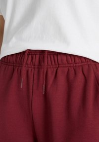Burgundy sweatpants med elastisk midja, utrustade med snörning för justerbar passform. Tyget verkar mjukt med en jämn textur.