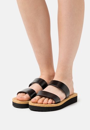 Sorte slip-in sandaler med to brede stropper, en korkfodsål og en tekstureret sort gummisål, med fladt design og åben tå.