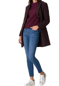 Pull côtelé bordeaux, manteau en laine foncé, jean skinny bleu et baskets argentées. Surfaces texturées et design épuré tout au long.