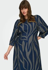 Vestido de color azul marino con un patrón de rayas onduladas en crema, con mangas abullonadas de tres cuartos y un escote redondo.