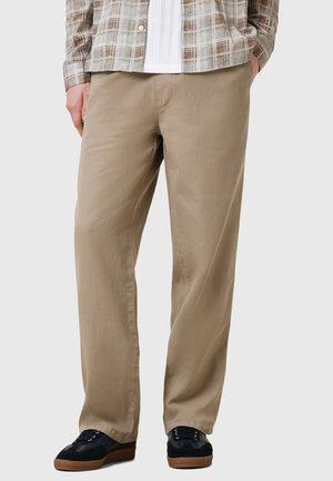 Pantaloni beige realizzati in tessuto leggero, caratterizzati da una vestibilità rilassata e da una texture liscia. Abbinati a sneakers scure per un contrasto.