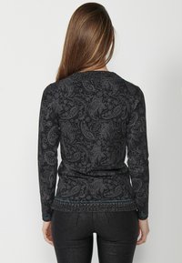 Pikkade varrukatega must sviiter, millel on paisley-muster, tekstuuriga kaelus ja elastne äär. Materjal näib olevat pehme ja sobib hästi kehakumerustega.
