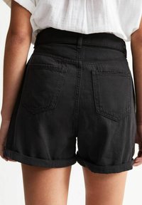 Black denim shorts with rolled cuffs, featuring two back pockets and a mid-rise waist, textured fabric, and simple stitching details.