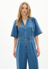 Jeans-Overall mit tiefem V-Ausschnitt, kurzen Puffärmeln und einem Reißverschluss vorne. Hat eine taillierte Taille und eine weit geschnittene Beinform.