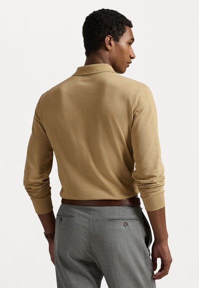 Bežs adīts puloveris ar ribotu apkakli un piedurknēm, apvienots ar pelēkajiem biksēm, kurām ir aizmugurējās kabatas un brūna josta. Gluda tekstūra.